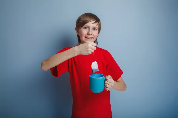 Boy teenager European appearance in a red shirt brown drops tea — Stock Photo, Image