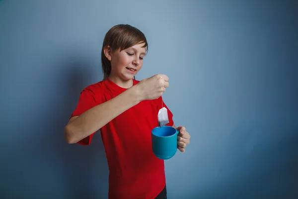 Boy teenager European appearance in a red shirt brown drops tea — Stock Photo, Image