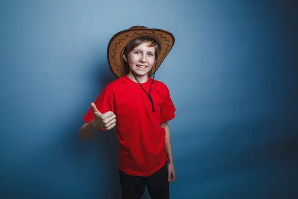 Boy teenager European appearance in a red shirt brown hat showin — Stock Photo, Image