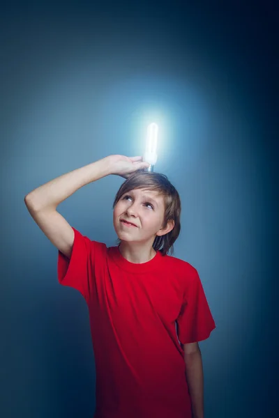 Dospívající chlapec drží žárovku nad hlavou na modré backgro — Stock fotografie