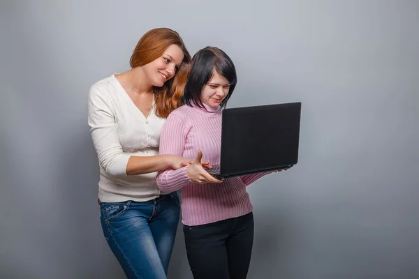 Två flickor europeiskt utseende ser ut i monitor och leende o — Stockfoto