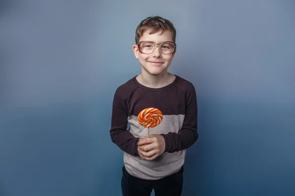 Europeo-looking ragazzo di dieci anni in occhiali leccare un lecca-lecca — Foto Stock
