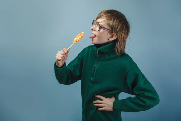 European-looking  boy of  ten years in glasses  licking a lollip — Stock Photo, Image