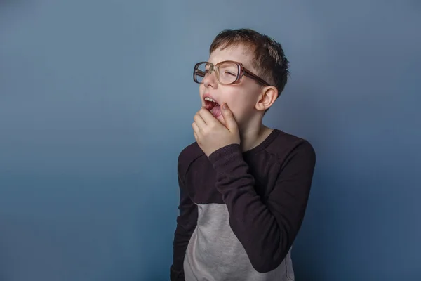 Европейский мальчик 10 лет в очках, зевающий на сером. — стоковое фото