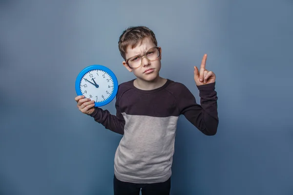 Europeiska-ser pojke på tio år i glas håller en vägg kloc — Stockfoto