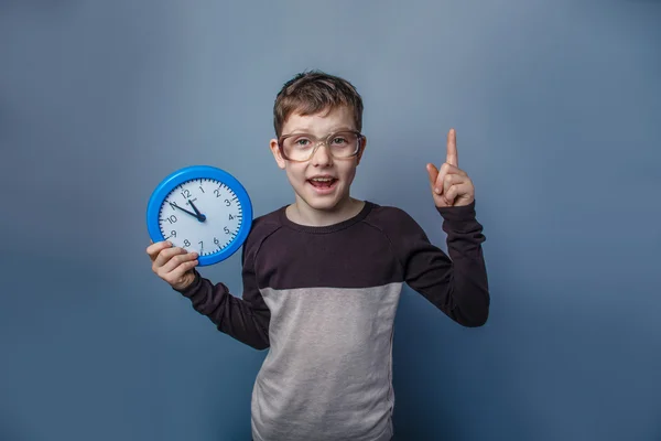 Europeiska-ser pojke på tio år i glas håller en vägg kloc — Stockfoto