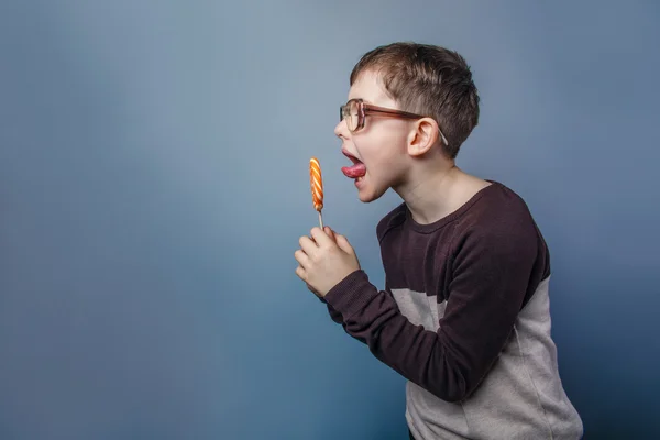 European-looking boy of ten years in glasses licking a lollipop — Stock Photo, Image