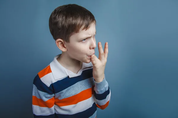 European-looking boy  of ten  years licks his finger on a gray b — Stock Photo, Image