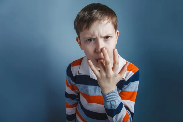 Europeu-olhando menino de dez anos lambe o dedo em um ba cinza — Fotografia de Stock