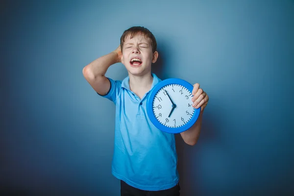 Teenager boy brown European appearance holds a clock closed his — Stock Photo, Image