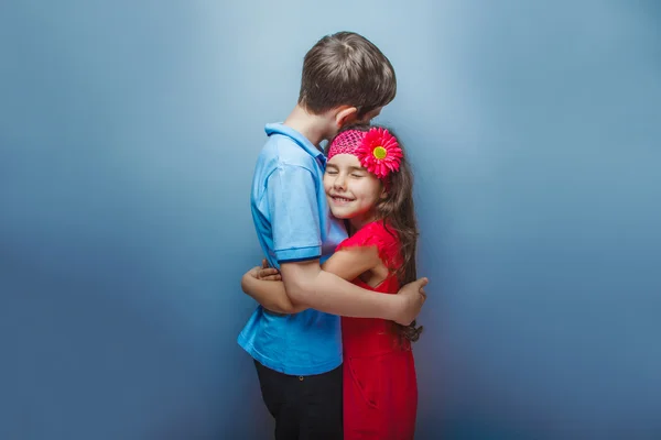 Дівчина-підліток обіймає хлопчика-підлітка на сірому фоні — стокове фото