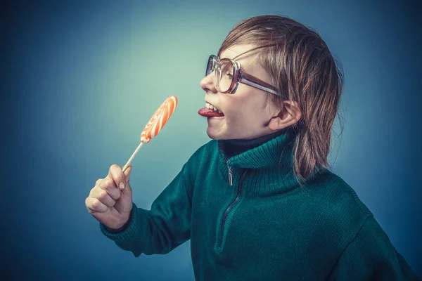 Europäisch aussehender Junge von zehn Jahren in Brille leckt einen Lutscher — Stockfoto