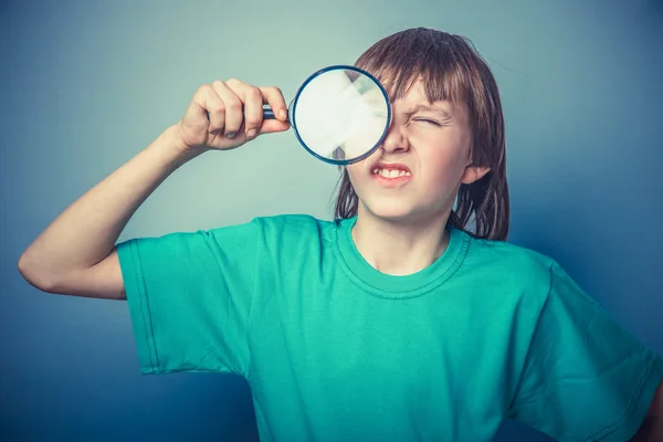 European-looking boy of ten  years holding a magnifying glass, a — Stock Photo, Image