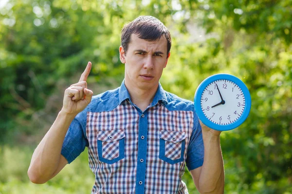 Uomo tenendo orologio mostrando pollici su uno sfondo verde estate — Foto Stock