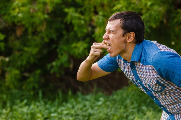 Человека на улице тошнит рвотой на зеленом фоне листьев — стоковое фото