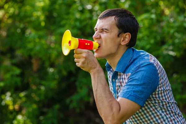 The man in the street holding a plastic speaker shouts on green — Stock Photo, Image