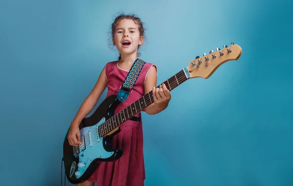 Ragazza aspetto europeo dieci anni a suonare la chitarra canta su un blu — Foto Stock