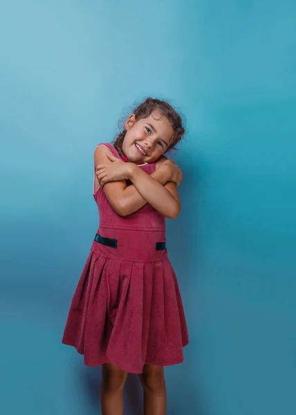 Girl European appearance decade hugging herself on a blue backgr — Stock Photo, Image