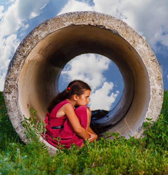 Homeless teenager girl sits on his haunches in the concrete pipe