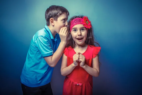 Teen boy whispering in the ear of teen girl on a gray  backgroun — Stock Photo, Image