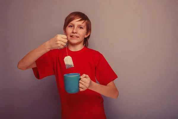 Ragazzo, adolescente, dodici anni in camicia rossa beve tè busta ret — Foto Stock