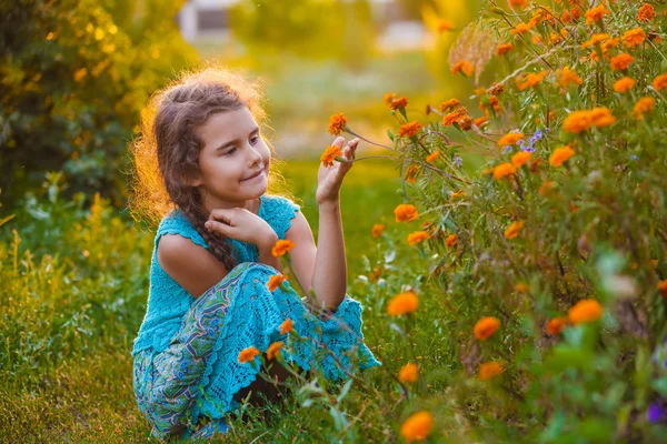 Teen girl sitting on his haunches and touching orange flower in — Stock Photo, Image