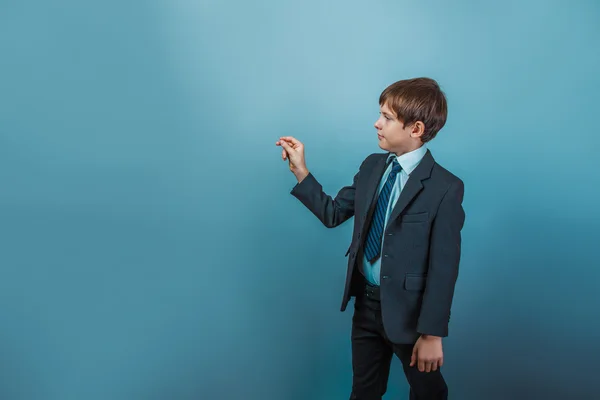 Ein zwölfjähriger Junge mit europäischem Aussehen in einem Anzug, der in die Luft schreibt — Stockfoto