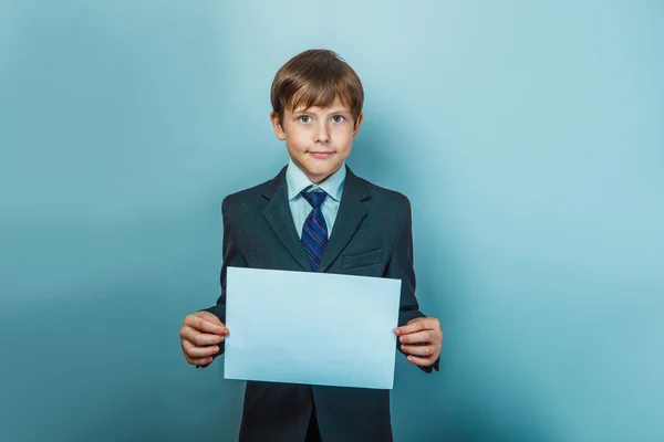 Ein zwölfjähriger Junge mit europäischem Aussehen in einem Anzug, der einen unbeschriebenen Blatt hält — Stockfoto
