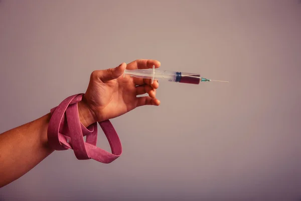 Hand with a plait holding a syringe with a drug on a gray backgr — Stock Fotó