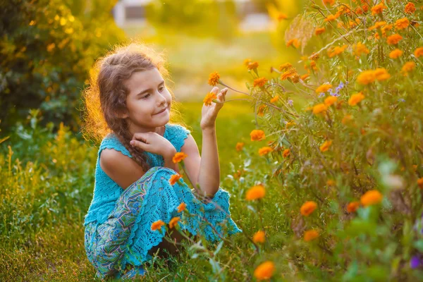 Teen girl sitting on his haunches and touching orange flower in — Stock Photo, Image