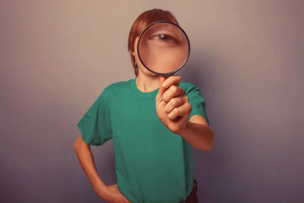 European-looking boy of ten years is looking through a magnifyin — Stock Photo, Image