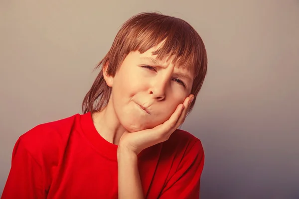 European-looking boy of ten years toothache, hand on cheek on a — Stock Photo, Image