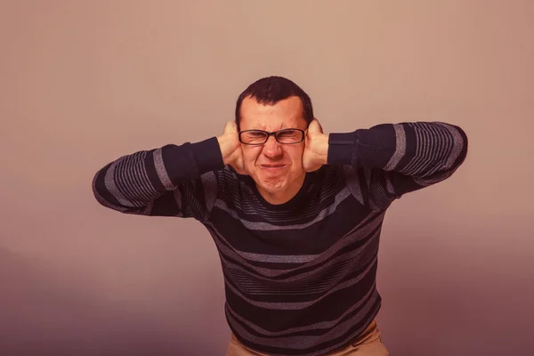 European-looking male of about thirty brunet covered his ears wi — Stock Photo, Image