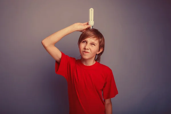 Boy teenager European appearance in a red shirt put a light bulb — Stockfoto