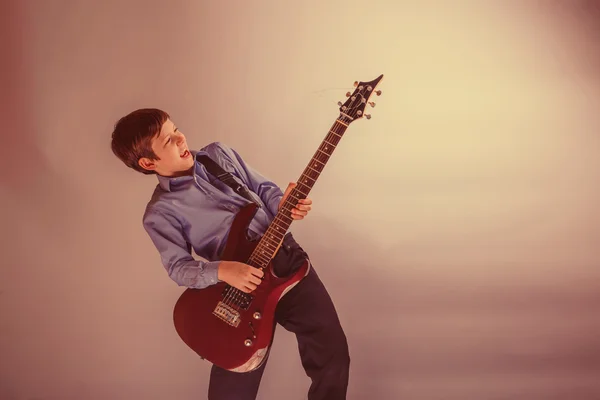 Adolescente ragazzo capelli castani aspetto europeo suonare la chitarra su un — Foto Stock