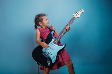 Girl seven years old, European-looking brunette in a pink dress playing guitar t closed her eyes on a gray background, music