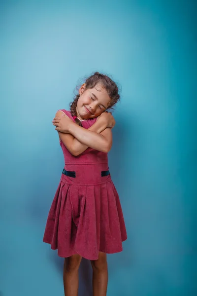 Girl seven years old, European-looking brunette in a pink dress hugging herself shoulders closed her eyes on a gray background, smiling, sleeping — Stockfoto