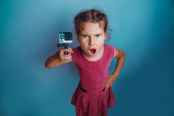 Teen girl child seven years, European appearance brunette holding action camera and opened her mouth on a gray background, anger, scream — Zdjęcie stockowe