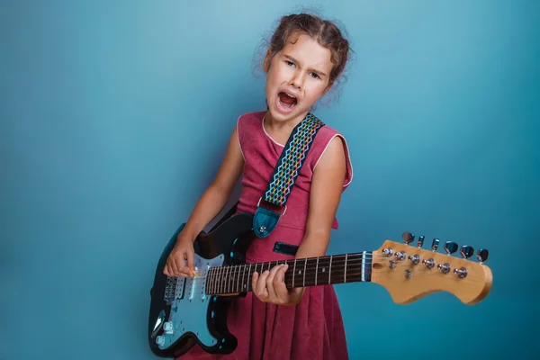 Ragazza adolescente bambino sette anni, aspetto europeo bruna in un abito rosa suona una chitarra su uno sfondo grigio, musica, canzone — Foto Stock