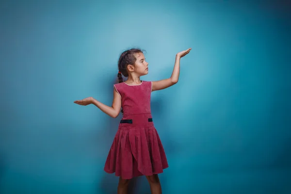 Ragazza adolescente bambino sette anni, aspetto europeo bruna in un abito rosa alzando le mani su uno sfondo grigio, posa, sorriso, est — Foto Stock