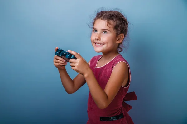 Girl seven years old, European-looking brunette in a pink dress holding a joystick and smiling on a gray background, happiness, joy, game Royalty Free Φωτογραφίες Αρχείου