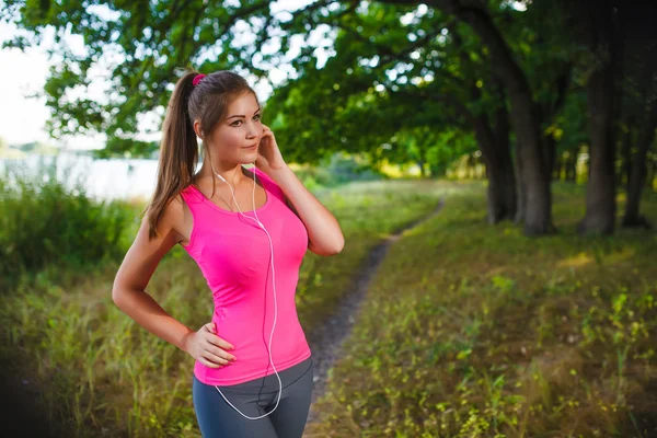 Woman running in green forest listening to music with headphones — ストック写真