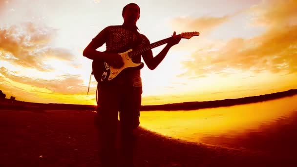 Narancssárga gitáros zenész ember kezd játszani a gitár sárga szűrő a folyó napnyugtakor ég felhők — Stock videók