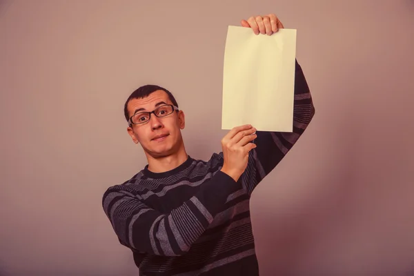 European-looking male holding a white sheet of paper on a gray b — Stock Photo, Image