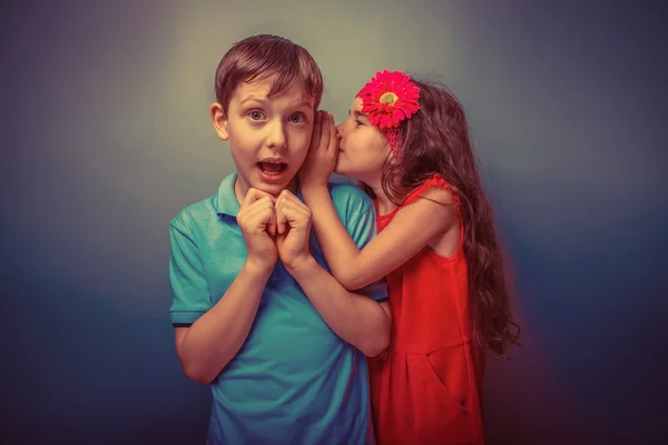 Teenage girl whispering in the ear of a secret teen boys on a  g — Stock Photo, Image