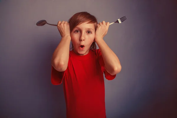 Adolescente in camicia rossa ragazzo dodici anni tenendo cucchiaio e forchetta , — Foto Stock