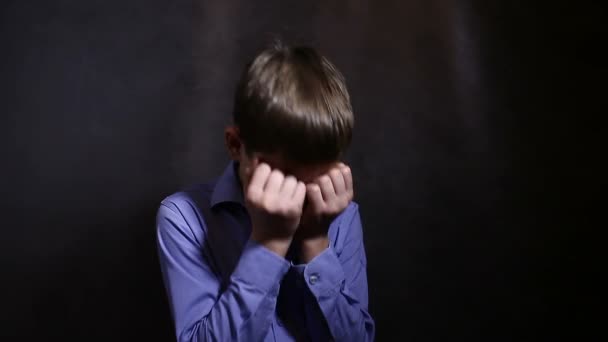 Adolescent garçon pleurer bouleversé fermé les yeux avec ses mains dans un bleu chemise, studio fond — Video