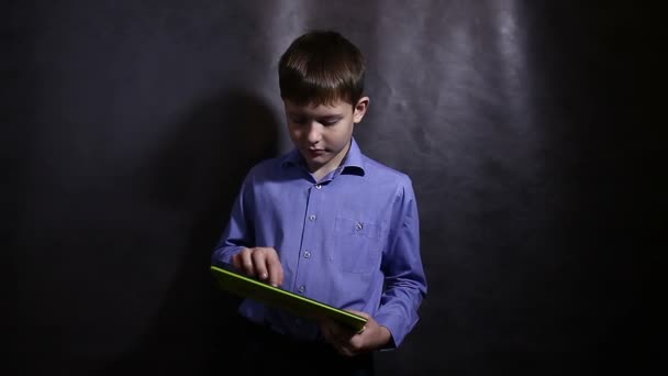 Tonårspojke i en blå skjorta spelar körs på den tablet mörka bakgrunden video — Stockvideo