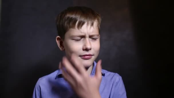 Tonårspojke i en blå skjorta innehar en tandvärk karies kinden mörk bakgrund video — Stockvideo