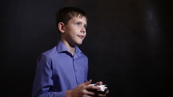 Tonårspojke i en blå skjorta, spelar en spelkonsol som innehar joystick mörka bakgrunden video — Stockvideo